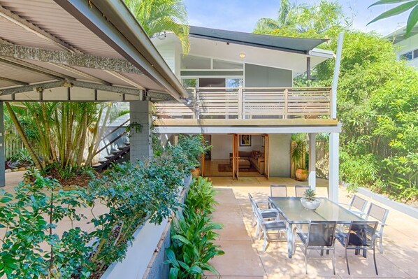 Une maison moderne dotée d’un balcon, d’un coin repas avec une table et des chaises, et d’un escalier menant à un étage supérieur.