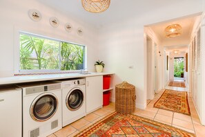A laundry room with two washing machines, a window with a view of greenery, and a hallway leading to a door. - Sunshine Beach House - Beautiful parts of nature (Sunshine Beach)