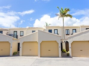 A row of residential buildings with garage doors, a palm tree, and a clear sky. - Weyba Quays Townhouse 7 Peza Court 6 (Noosa Heads)