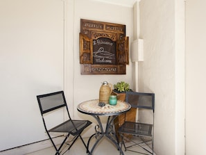 A small outdoor seating area with two metal chairs and a round table, a decorative wooden sign above, and a potted plant on the table. - Weyba Quays Townhouse 7 Peza Court 6 (Noosa Heads)