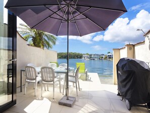 An outdoor patio with a table and chairs, a large umbrella, and a grill. - Weyba Quays Townhouse 7 Peza Court 6 (Noosa Heads)