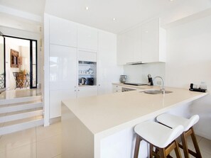 Una cucina moderna con mobili bianchi, una grande isola con sgabelli da bar e una scala che conduce in un'altra zona.