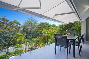A balcony with a table and chairs, overlooking a lush garden and trees.