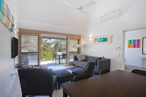 A modern living room with a sofa, chairs, a table, and a TV.