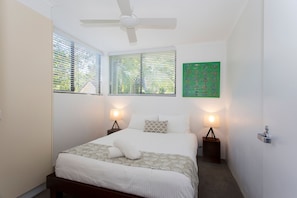 A bedroom with a bed, two bedside tables with lamps, a ceiling fan, and a green artwork on the wall. - Headland Views 5 Alderly Terrace 42 (Noosa Heads)
