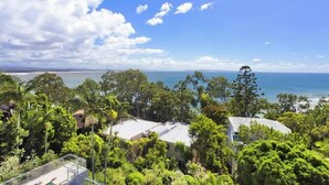 A coastal property with a pool, surrounded by lush greenery and a view of the sea.