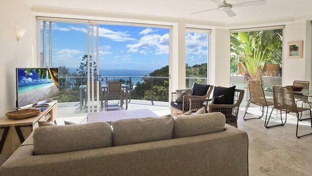 A spacious living area with a large window offering a view of the ocean, a comfortable sofa, and a dining table with chairs.