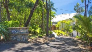 A stone sign with '25 Allambi' and a pathway leading to a building surrounded by lush greenery.