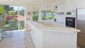A modern kitchen with a large island, stainless steel appliances, and a view of greenery outside.