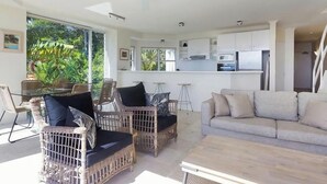 A modern kitchen with white cabinets, a dining area with wicker chairs, and a large window with a view of greenery.