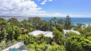 A residential area with a pool, surrounded by lush greenery and overlooking a coastal view.