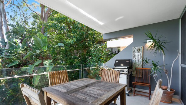 An outdoor patio with a wooden table and chairs, a barbecue grill, and potted plants.