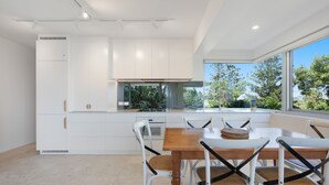 A modern kitchen with white cabinetry, a dining table with chairs, and a view of greenery outside.