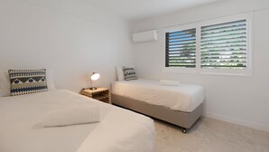 A bedroom with two beds, a ceiling fan, an air conditioning unit, and a window with blinds.