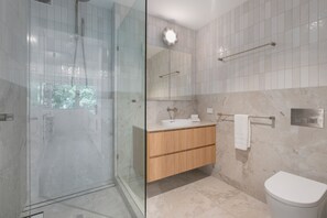 Un baño moderno con cabina de ducha de vidrio, tocador de madera, lavamanos de mármol y un inodoro.