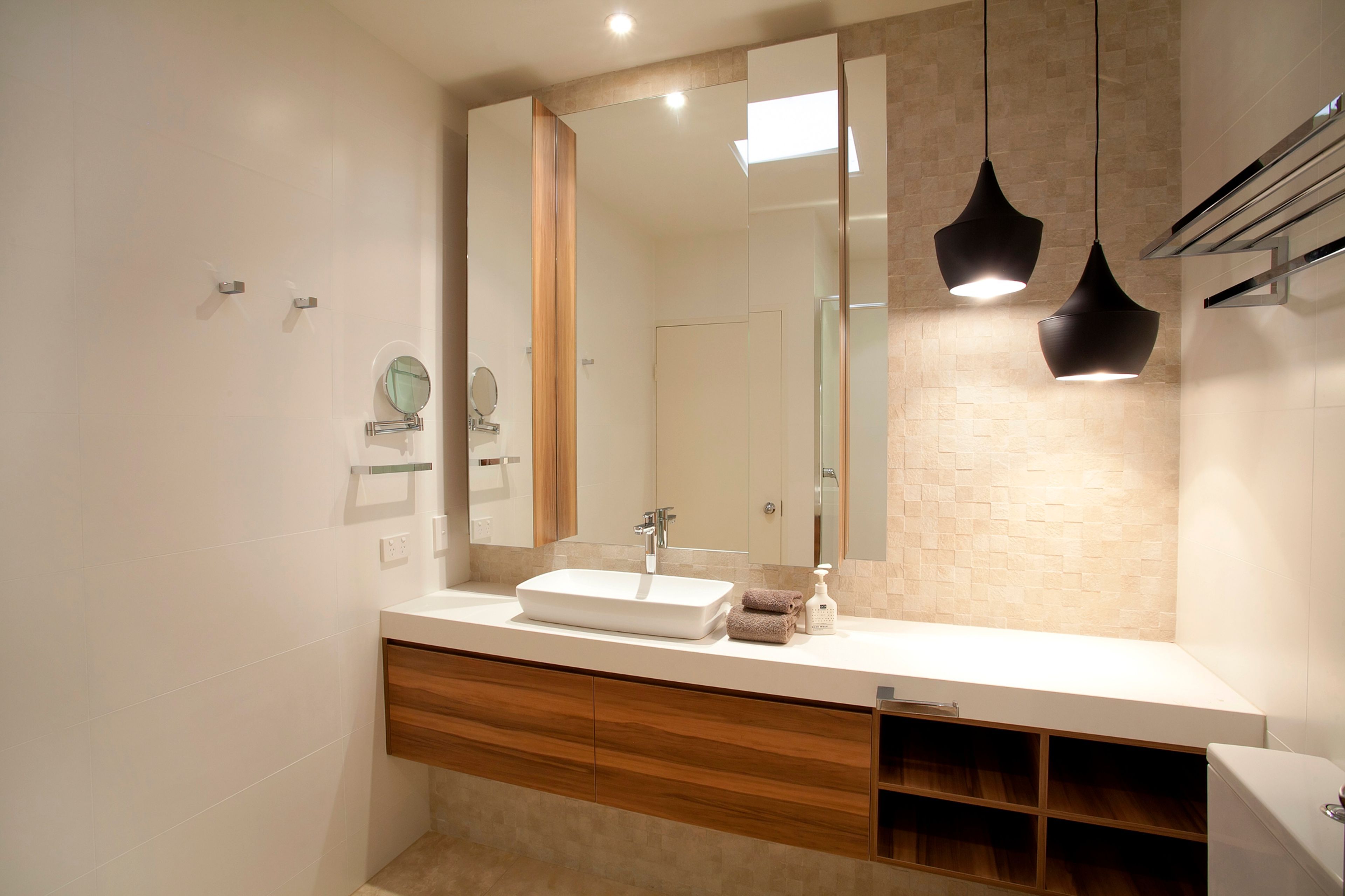 A modern bathroom with a large mirror, a white sink, wooden cabinetry, and pendant lighting.
