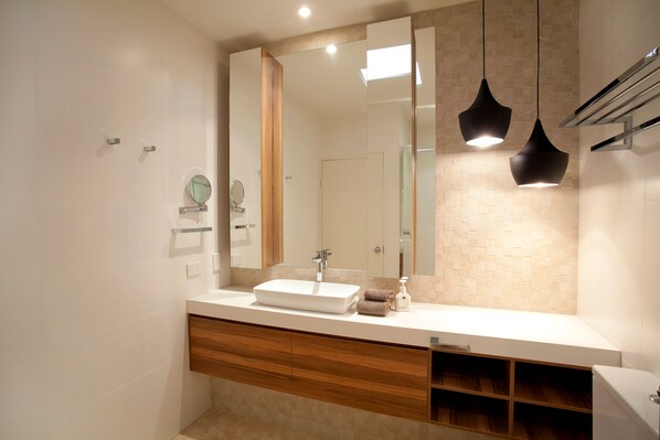 A modern bathroom with a large mirror, a white sink, wooden cabinetry, and pendant lighting.