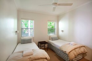 A room with two single beds, a ceiling fan, and windows with blinds.