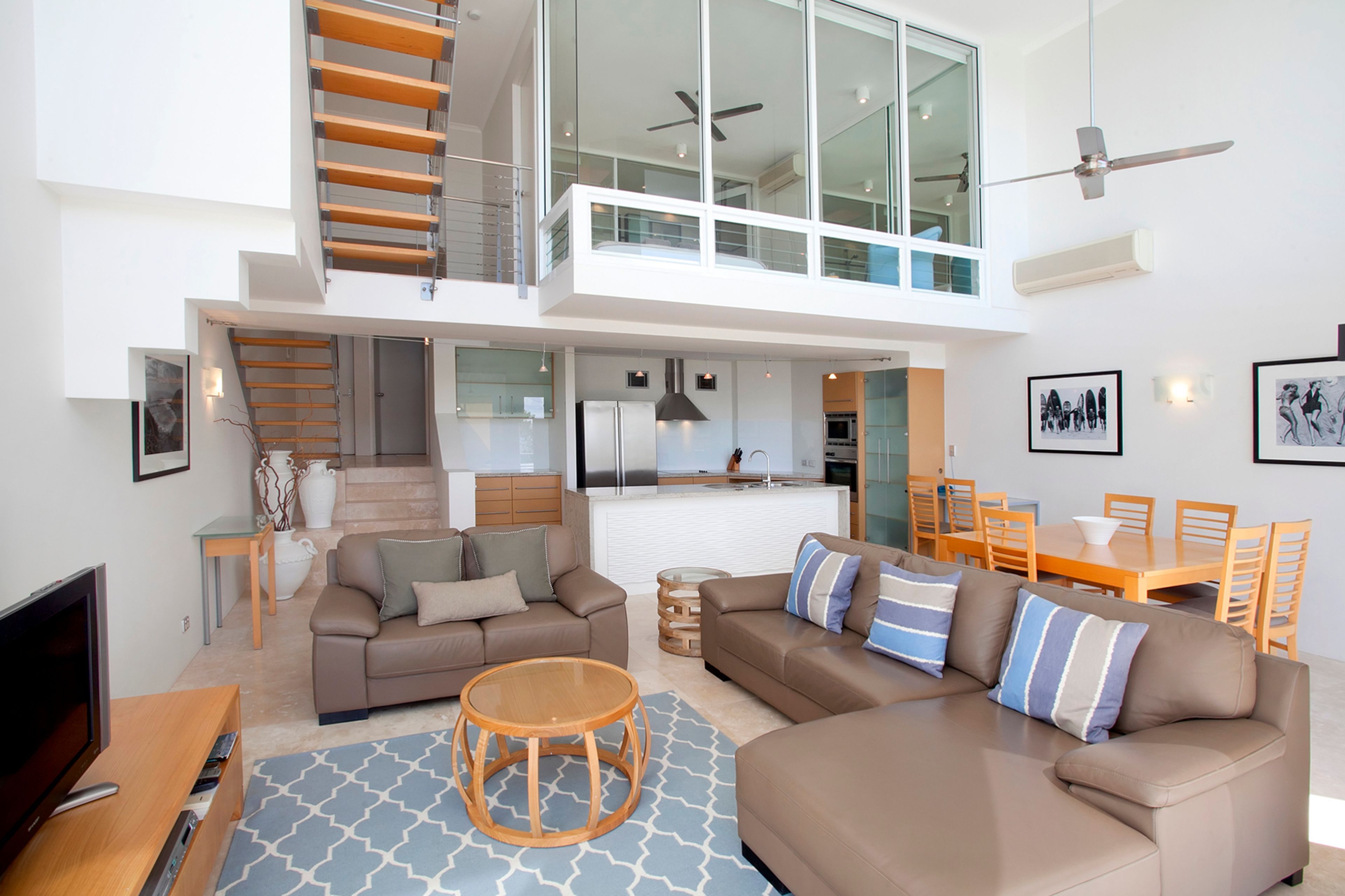 Un appartement moderne comprenant un salon, un coin repas, une cuisine et un escalier menant à l’étage supérieur.