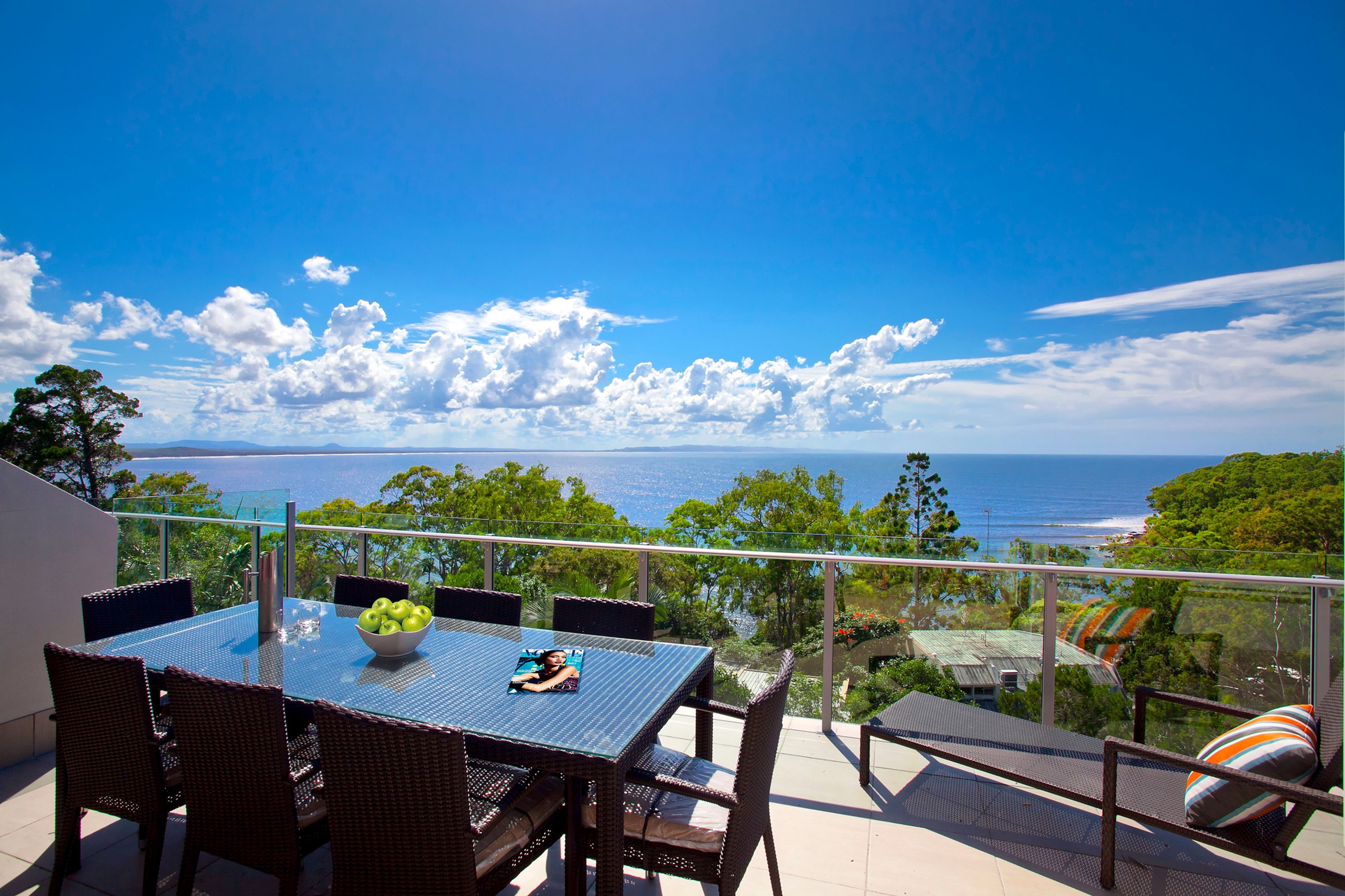 A balcony with a table, chairs, and a bowl of fruit.