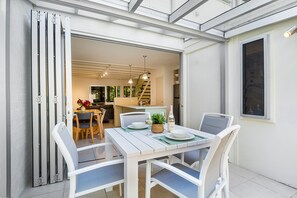 Een eethoek met een tafel gedekt voor twee personen, stoelen, een potplant en een fles wijn.