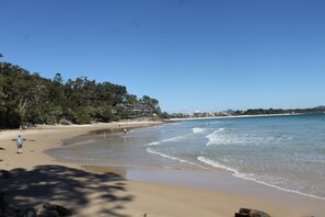 Una playa con cielos despejados, orilla arenosa y zona boscosa al fondo.