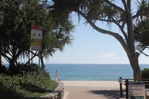 Een strandpad dat naar de oceaan leidt, met een bord waarop Noosa Heads SLSC staat.