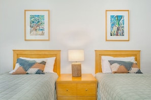 A hotel room with two beds, a nightstand with a lamp, and two framed artworks on the wall.