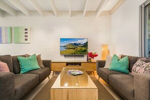 Een moderne zithoek met twee banken, een salontafel, een flatscreen televisie en een schilderij aan de muur.