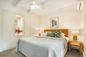 Habitación de hotel con cama, lámparas de noche, mesita de noche, espejo, ventilador de techo y un cuadro en la pared.