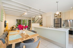 Een moderne keuken met een centraal eiland, roestvrijstalen apparatuur en een eethoek met een tafel gedekt voor twee personen.