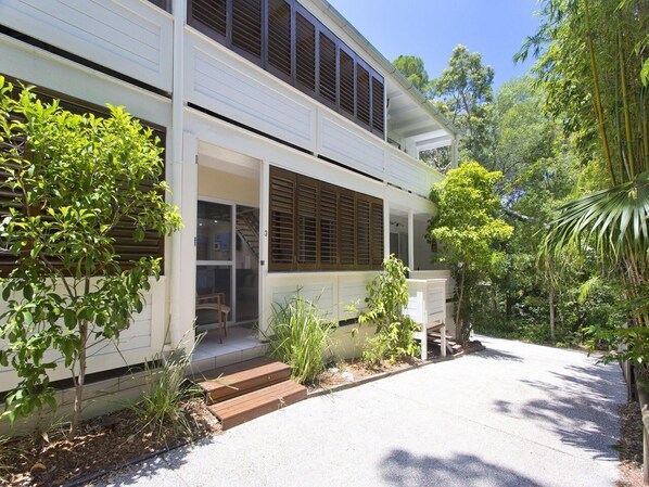 A two-story house with a covered porch, a driveway, and surrounding greenery.