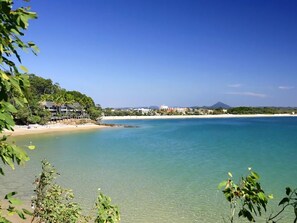 A coastal view with clear water, a beach, and buildings in the background.