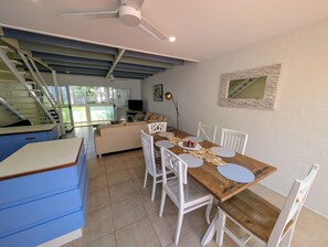 Zona pranzo con tavolo in legno, sedie bianche e una cucina sullo sfondo.