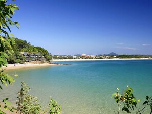 Paesaggio costiero con acque limpide, una spiaggia e una montagna all'orizzonte.