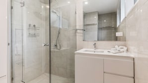 Un baño moderno con cabina de ducha de vidrio, un lavabo blanco y un espejo grande.