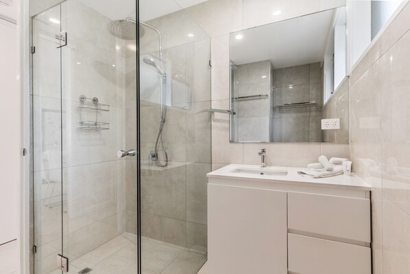 A modern bathroom with a glass shower enclosure, a white sink, and a large mirror.