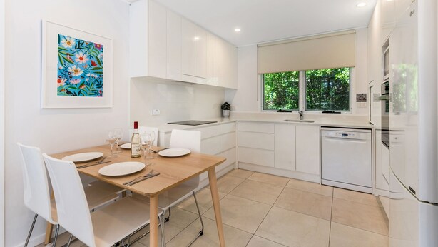 Una cocina moderna con armarios blancos, una mesa de comedor con sillas y un ventanal con vistas a zonas verdes.