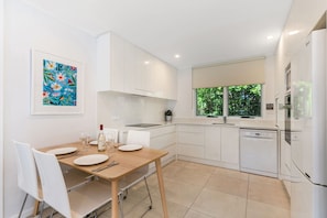 A modern kitchen with white cabinetry, a dining table with chairs, and a window with a view of greenery.