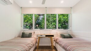 Un dormitorio con dos camas individuales, un escritorio y una ventana con vistas a árboles.