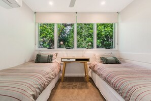 Een slaapkamer met twee eenpersoonsbedden, een bureau en een raam met uitzicht op bomen.