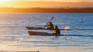 Un atardecer sobre una superficie acuática tranquila con dos canoas.