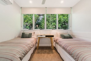 A bedroom with two single beds, a desk, and a large window with a view of greenery.