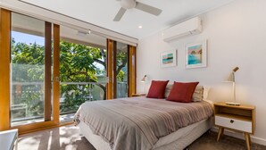 Un dormitorio con una cama grande, una mesita de noche, un ventilador de techo y vistas al exterior.