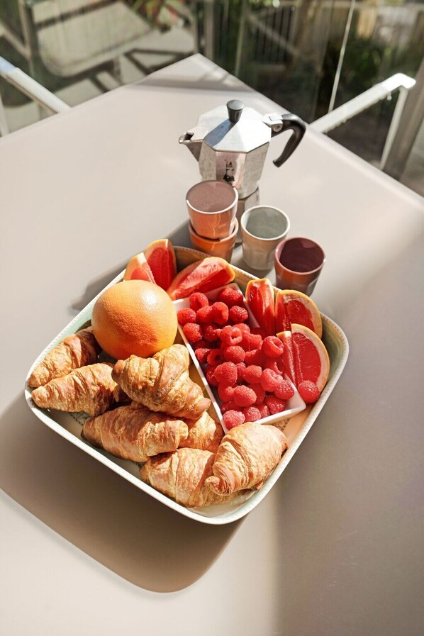 A tray of food including croissants, oranges, raspberries, and a pitcher of coffee on a table.