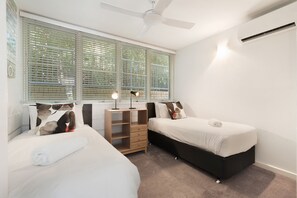 Ein Schlafzimmer mit zwei Betten, einem Deckenventilator, einem Fenster mit Jalousien und einer Nachttischlampe.