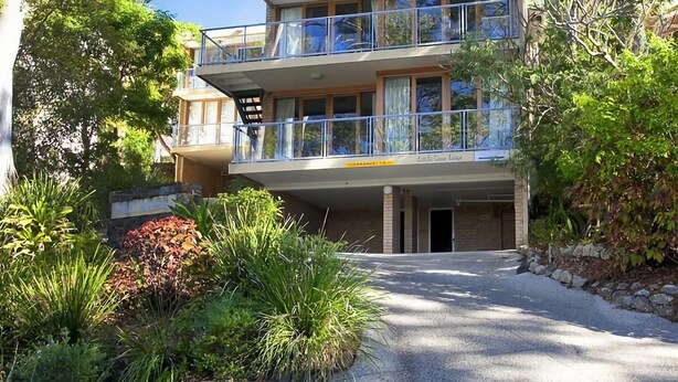 Un immeuble à plusieurs étages doté de balcons, un ciel dégagé et une végétation luxuriante tout autour.