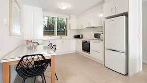 Une cuisine moderne avec des meubles blancs, une table à manger avec des chaises, un réfrigérateur et un four à micro-ondes.