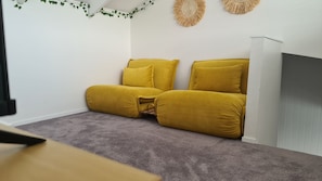 Una stanza con tappeto grigio, parete bianca e divano giallo.