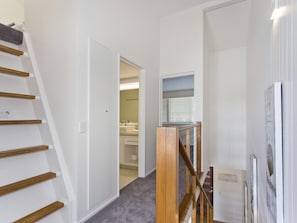 A hallway with a wooden staircase, a door leading to a bathroom, and a wall-mounted light fixture.